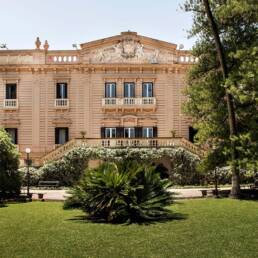 Elegant villa with Mediterranean architecture surrounded by a lush, serene garden and palm trees.