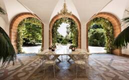 Serene outdoor dining oasis with terracotta arches, lush greenery, and elegant rustic furnishings.