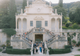 Elegant outdoor wedding celebration at a villa, featuring guests in formal attire and lush scenery.